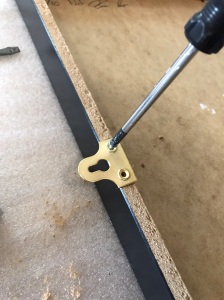 Close-up of a mirror plate being screwed to a frame with a manual screwdriver